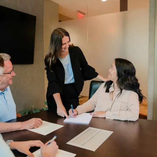 Four professionals engaged in a meeting, smiling and discussing ideas around a conference table with documents and pens.