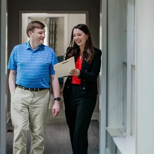 Two colleagues walking down a hallway discussing documents with smiles in a professional office setting