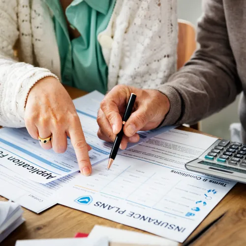 Two people reviewing insurance plans and application forms with a calculator on wooden table