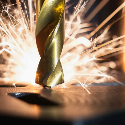 Close-up of a drill bit cutting metal with bright sparks flying around in a workshop setting.
