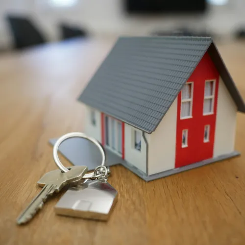 House model with red and white walls and a keychain with house-shaped key on wooden surface.