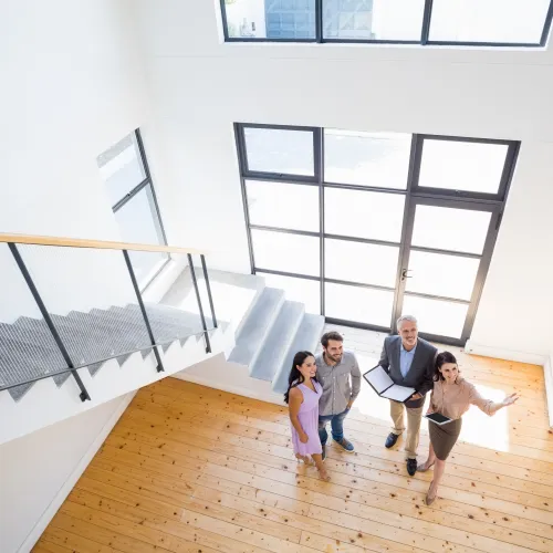 Real estate agents showing a young couple a bright modern home with wooden floors and large windows.