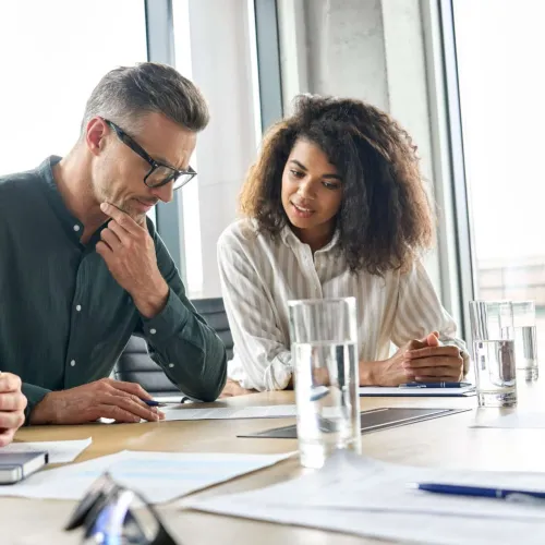 Three colleagues engaged in a discussion around a table with documents and glasses of water in a modern office.