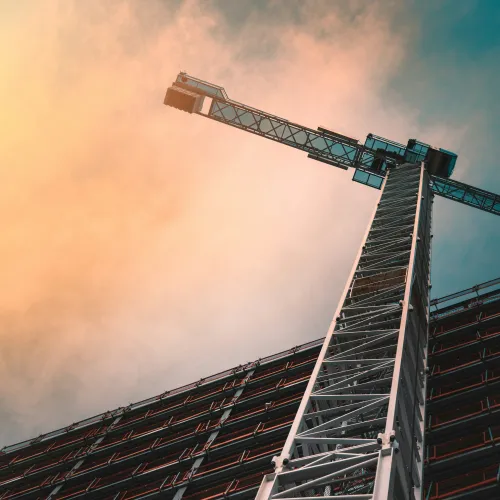 Construction crane towering over a building under a dramatic sunset sky with orange and blue hues.