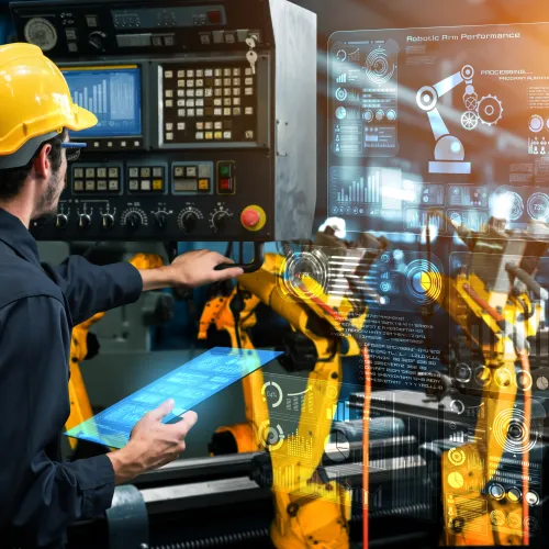 Engineer with hard hat controls robotic arms using digital interface and tablet in advanced automation factory.