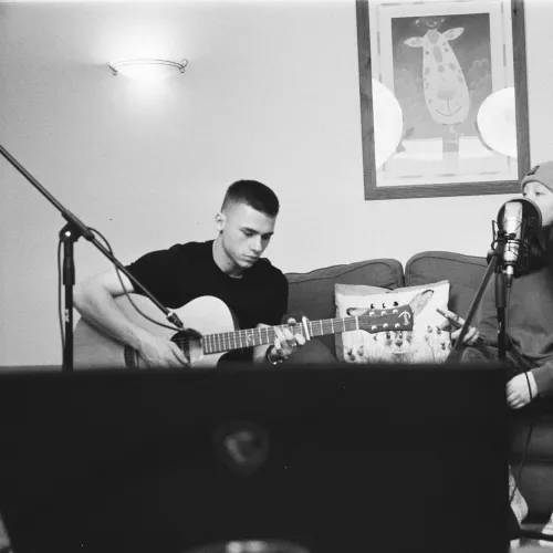 a man playing guitar next to a man sitting on a couch