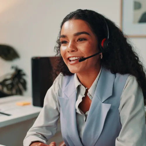 Smiling female customer service representative wearing headset at desk with computer in modern office.