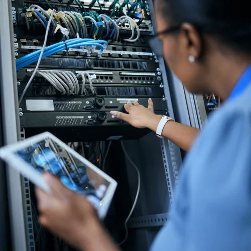 Technician working on server rack with network cables and holding a digital tablet in data center environment