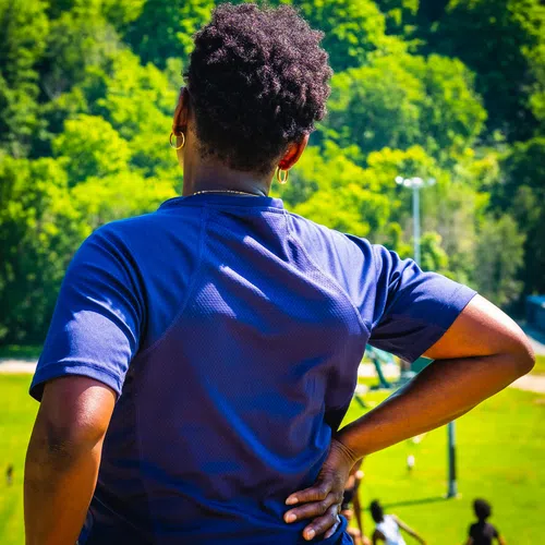 Person with hands on hips looking at people playing sports on a sunny day in a green park