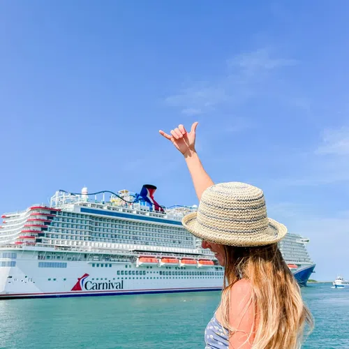 Woman in sunhat gestures shaka sign near a large Carnival cruise ship on clear blue sea under bright sky