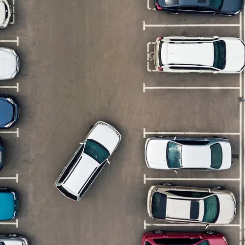 Overhead view of a parking lot with cars parked and one car maneuvering between rows of vehicles.