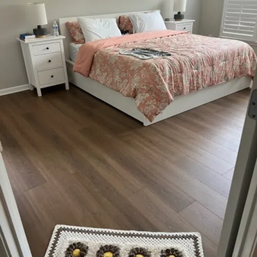 Cozy bedroom with white furniture, floral pink bedspread, wooden floor, and a crocheted rug near the door.