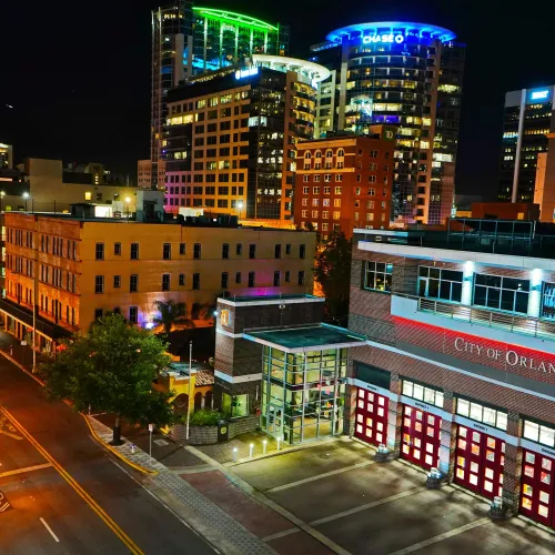 Nighttime cityscape of Orlando featuring the City of Orlando Fire Station and illuminated high-rise buildings.
