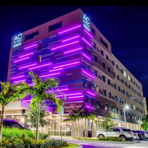 AC Hotels Marriott building lit with vibrant purple neon lights at night surrounded by palm trees and parked cars.