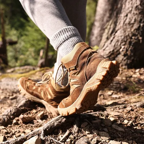 Close-up of brown hiking boots on rocky forest trail with tree roots and greenery in background