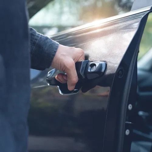 Person opening a black car door with hand gripping the handle in soft natural light.