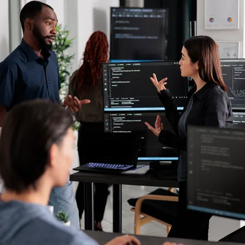 Software developers collaborating and coding in a modern office with multiple monitors displaying code.