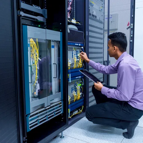 IT technician working on server racks connecting cables while holding a tablet in a data center room