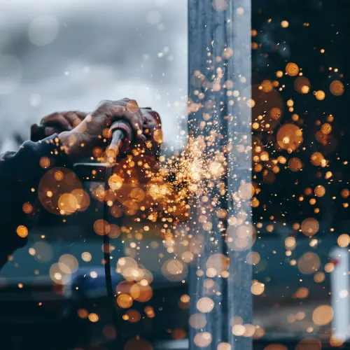 Worker using grinder tool creating bright orange sparks during metalwork outdoors.