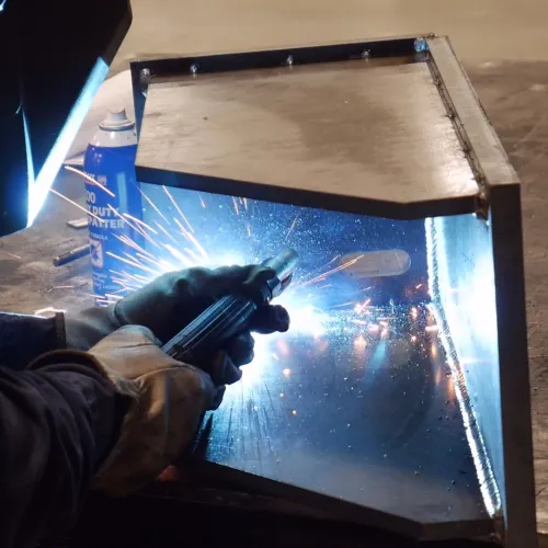 Welder in protective gear welding metal frame with bright sparks in workshop environment.