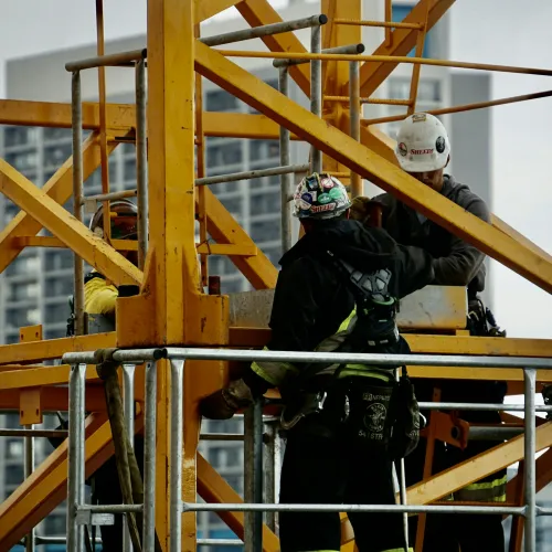 Construction workers in safety gear on a yellow scaffolding structure at a building site.