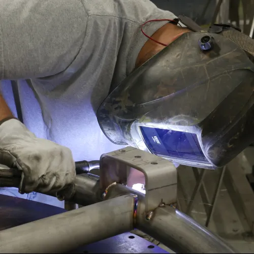 Welder wearing protective helmet and gloves welding metal pipes in industrial workshop.