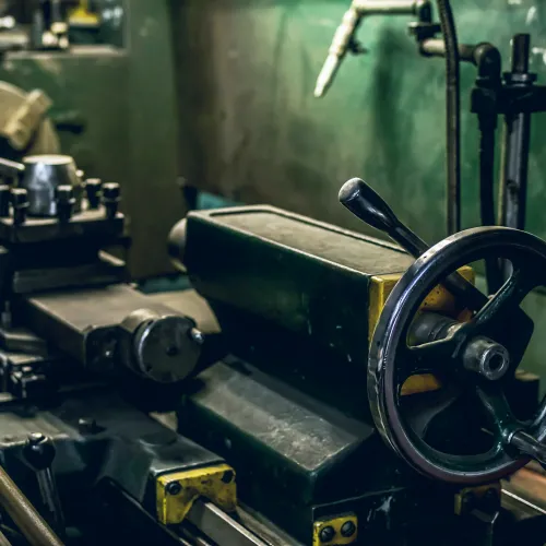 Close-up of a metal lathe machine with handwheel and mechanical components in a workshop setting