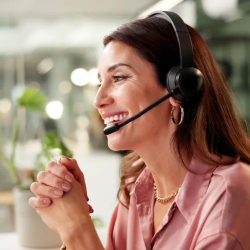 Smiling woman wearing headset working at computer in modern office with blurred background