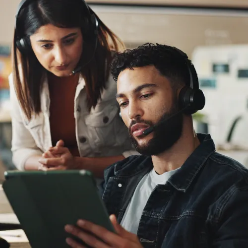 Man with headset and woman collaborating over tablet in modern office workspace