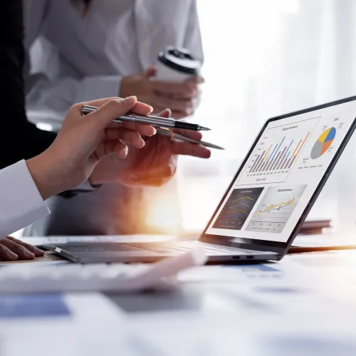 Business team analyzing financial data charts on a laptop during a collaborative meeting in a bright office.