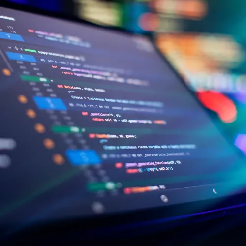 Close-up of computer screen displaying colorful lines of programming code in a dimly lit environment.