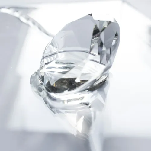 Close-up of a large clear faceted crystal diamond resting on a reflective white surface.