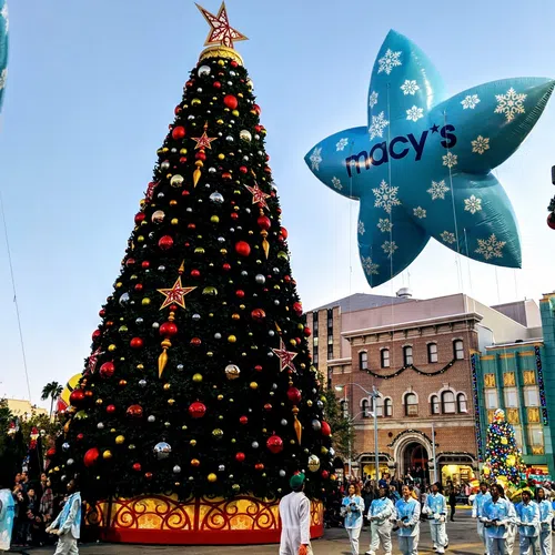 Large decorated Christmas tree and Macy's star balloon during festive holiday parade with crowd and performers.