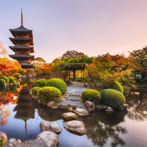 Serene Japanese garden with stone pathway, lush greenery, and pagoda at sunset reflecting on still pond water.