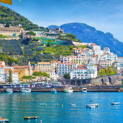 Scenic Amalfi Coast with colorful buildings, boats on blue water, green hills, and lemon tree in foreground