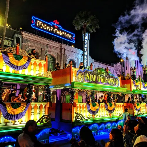 Illuminated Miss New Orleans parade float decorated with lights and crowds at night during a street festival.