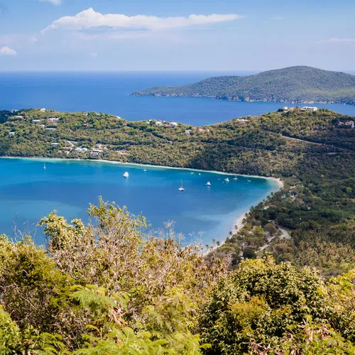 Aerial view of lush green islands with clear blue waters of Meagans Bay and sailboats under a partly cloudy sky.