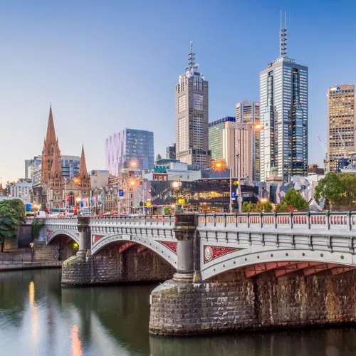 Melbourne city skyline with historic bridge and river at dusk reflecting city lights and buildings.
