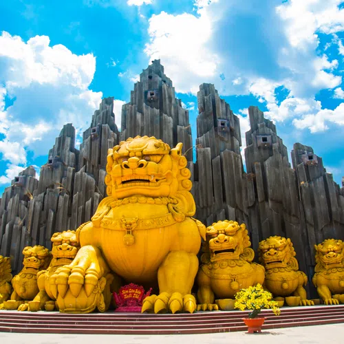 Golden lion statues in front of tall, jagged stone formations under a bright blue sky with clouds.