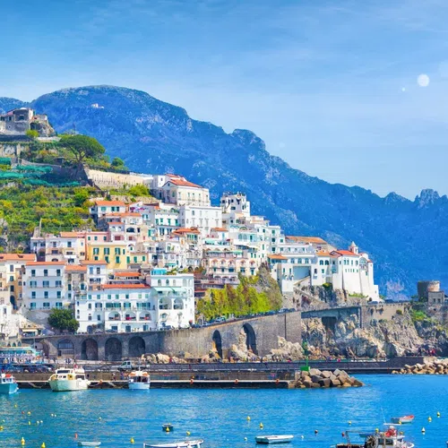 Scenic Amalfi Coast with colorful cliffside buildings, boats in turquoise water, and lemon tree branches in foreground