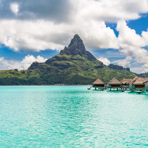 Turquoise lagoon with overwater bungalows and a mountain under a partly cloudy sky in a tropical island setting in Bora Bora