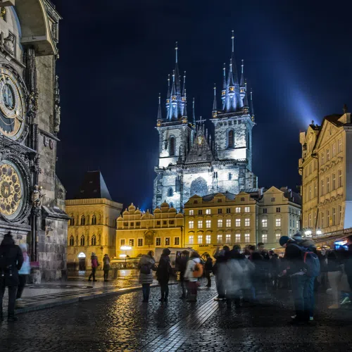 Crowded Old Town Square at night with Prague Astronomical Clock and illuminated Church of Our Lady before Týn