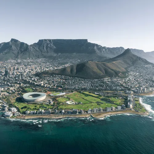 Aerial view of Cape Town with Table Mountain, Lion's Head, cityscape, and coastal shoreline under a clear sky.