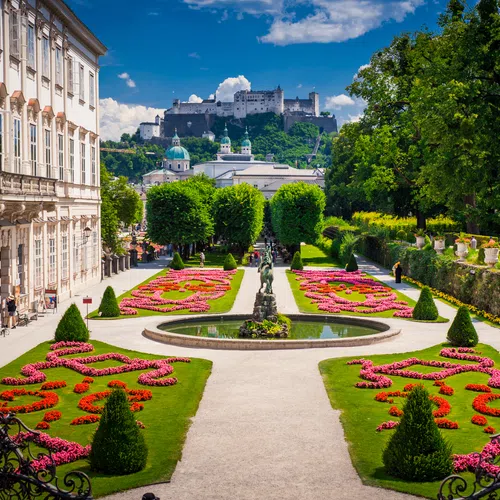 Beautiful Mirabell Gardens in Salzburg with colorful flowerbeds and Hohensalzburg Fortress in the background under blue sky