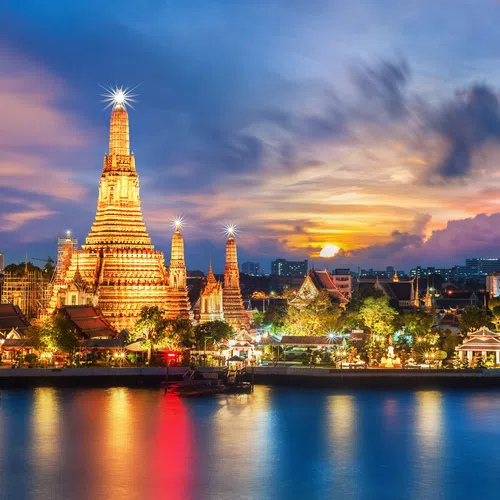 Wat Arun temple illuminated at sunset with reflections on the Chao Phraya River in Bangkok, Thailand