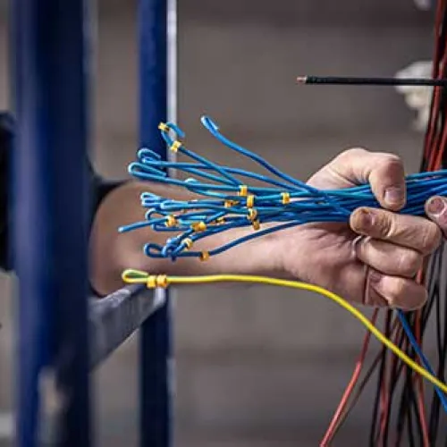 Electrician organizing multiple blue wires with labeled ends while working on electrical panel.