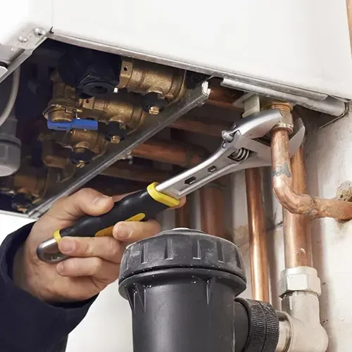 Close-up of plumber using adjustable wrench to tighten copper pipes under a boiler system.