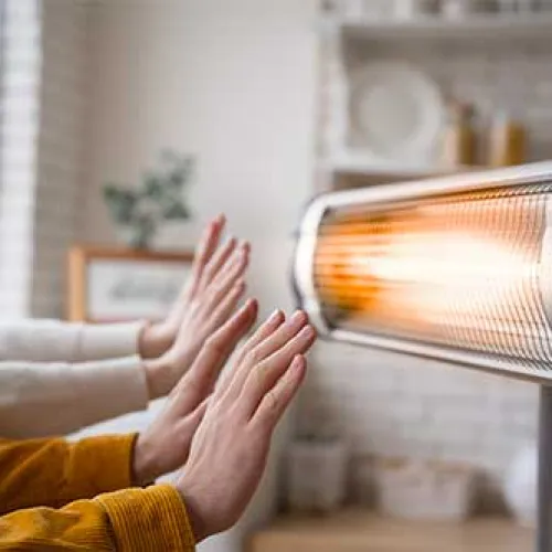 Two people warming hands in front of an electric heater in a cozy indoor setting.