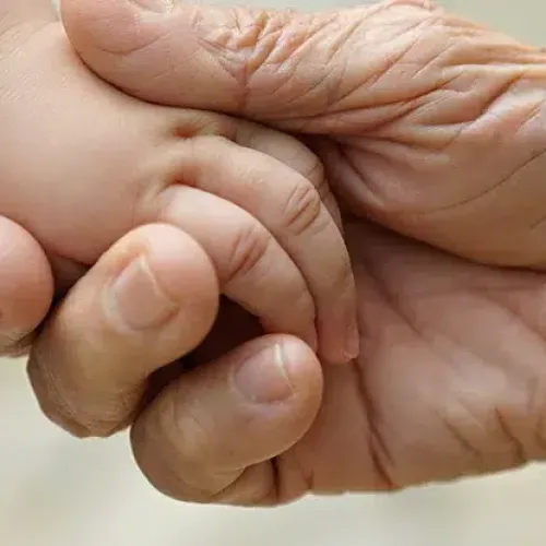 Close-up of elderly hand gently holding a baby's hand symbolizing care and connection.