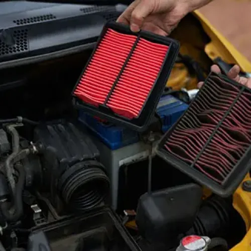 Person holding new and old car air filters over engine bay during vehicle maintenance